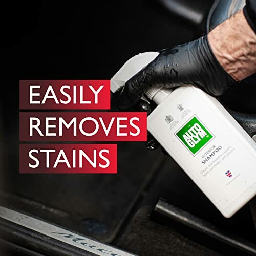 Person using Autoglym shampoo spray for stain removal in car interior.